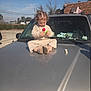 boots, brick, building, car, casual_clothing, child, curiosity, curly_hair, daylight, hood, nature, outdoor, paper, parking_lot, person, sky, toddler, toy, vehicle, window