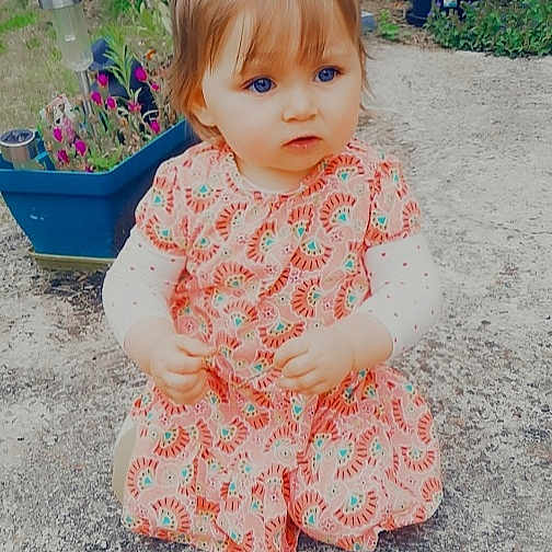 Norah participe au concours pour gagner de l'argent avec cette photo : baby, cheek, child, dress, face, outerwear, pattern, peach, pink, play, sitting, skin, sleeve, smile, toddler