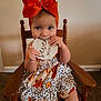 Evelyn joined the competition — help win amazing prizes! baby, child, infant, girl, orange_bow, wooden_chair, floral_dress, carpet, wall, milestone_sign, cute, portrait, indoor, smiling, hands, face, sitting, headwear, decorative, young