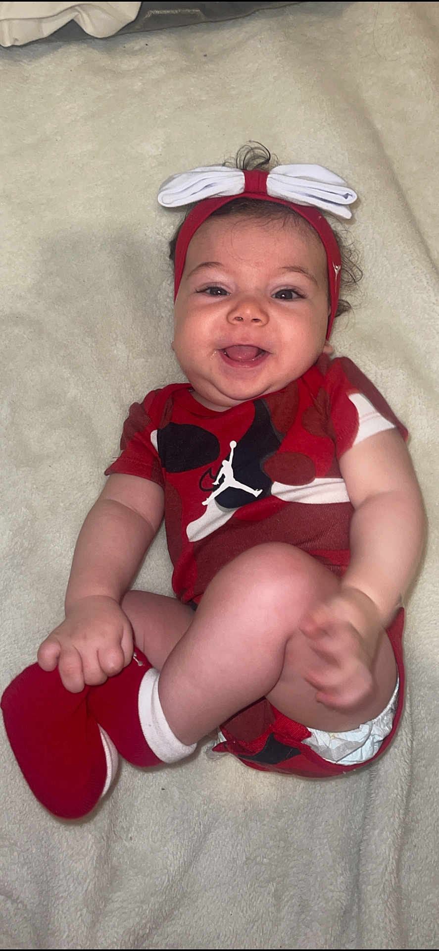 Lina participe au concours pour gagner de l'argent avec cette photo : baby, smiling, headband, bow, red_clothing, socks, diaper, blanket, infant, happy, cute, child, lying_down, playful, face, human, one_person, indoors, skin, closeup