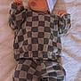 baby, infant, checkered_clothing, hat, beanie, lying_down, blanket, soft_texture, cute, tongue_out, cozy, warm_clothes, newborn, child, socks, small_hands, relaxed, indoors, portrait, sleepwear
