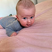 Mathias is registered to the contest to win money with this photo: baby, bedroom, child, cozy, cute, expression, eyes, face, gray_onesie, hand, head, indoors, infant, lying_down, person, pink_blanket, skin, smile, soft_texture, young_child