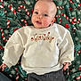 baby, infant, blanket, candy_cane_pattern, white_sweatshirt, text_on_clothing, hearts, gray_pants, lying_down, face, smiling, cute, cozy, festive, holidays, indoor, child, person, soft_texture, pacifier