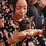 black_dog, braided_hair, child, close_up, cozy, cute, dog, gingerbread_man, hand, headband, holiday_theme, indoor, pajamas, person, phone, plush_toy, relaxed, seated, smiling, toy