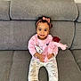 cartoon_cat, casual_clothing, child, cute, flower, gray_couch, happy, headwear, home, indoor, pants, pink_headband, pink_sweatshirt, portrait, rose, sitting, smile, socks, toddler, young_child