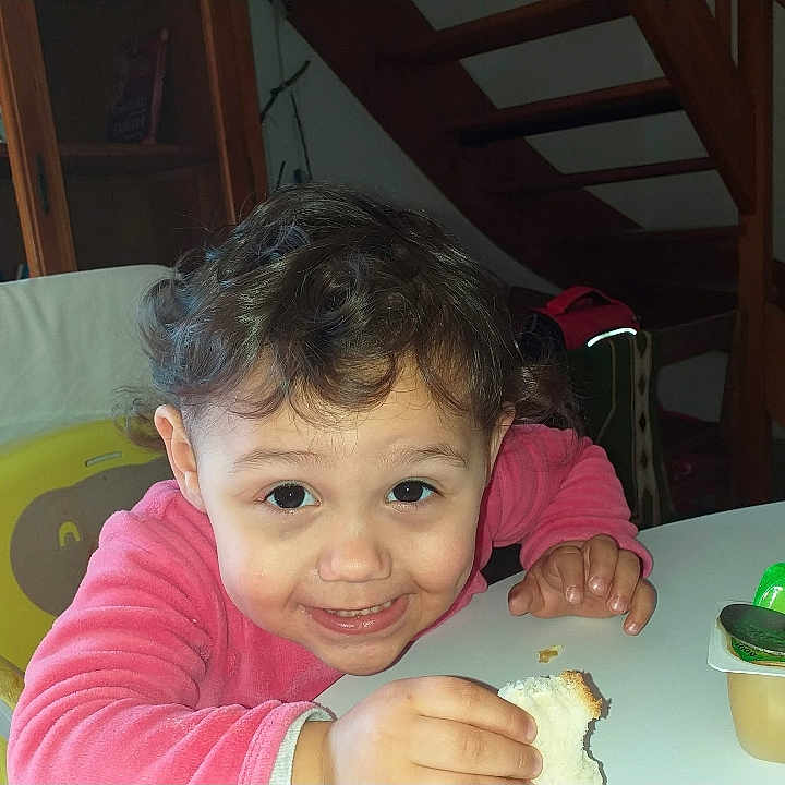 Neyssen participe au concours pour gagner de l'argent avec cette photo : bread, chair, child, curly_hair, cute, face, food, furniture, happy, home, indoor, person, pink_sweater, portrait, smiling, snack, staircase, table, toddler, young_child