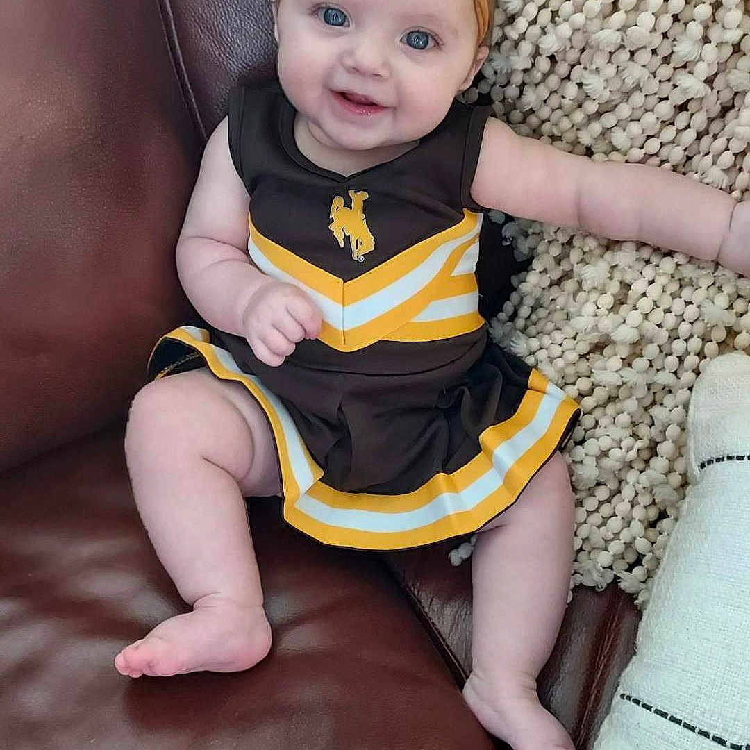 Emmylia is registered to the contest to win money with this photo: baby, babylaughing, chair, clothing, costume, couch, cushion, dress, face, furniture, happy, head, homedecor, pants, person, photography, portrait, sitting, smile, t_shirt