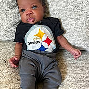Zyair joined the competition — help win amazing prizes! baby, infant, child, couch, clothing, black_shirt, gray_pants, person, portrait, indoors, sitting, cute, face, expression, young_child, home, relaxed, soft_fabric, footwear, necklace