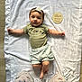 baby, infant, blanket, headband, flower, green_shirt, shorts, wooden_sign, text, floor, legs, floral_pants, toddler, lying_down, indoors, cute, child, person, soft_texture, home
