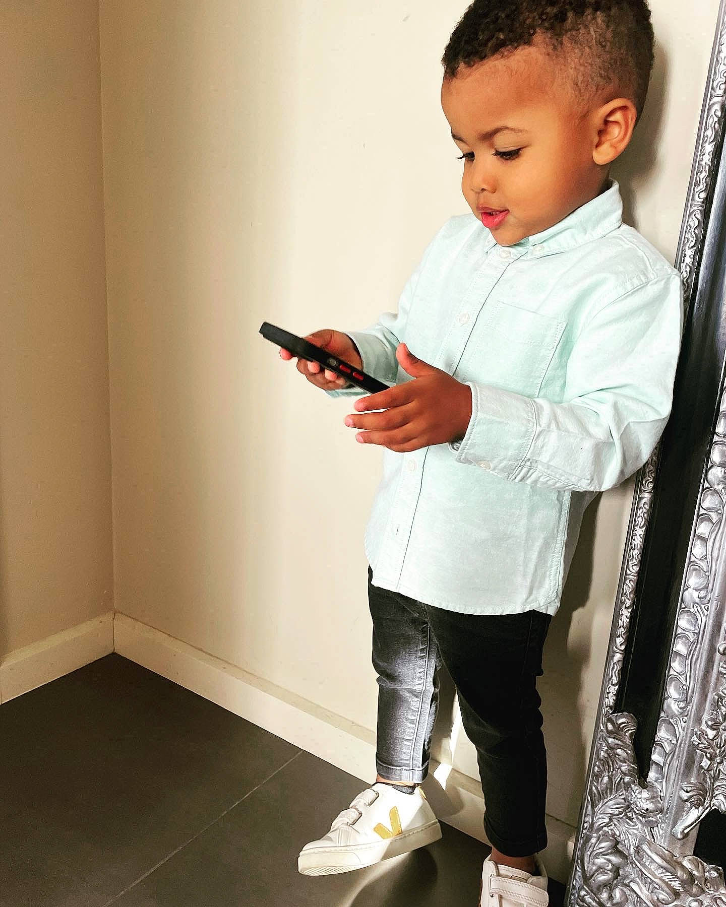 Edoardo is registered to the contest to win money with this photo: baby_toddler_clothing, collar, denim, door, dress_shirt, elbow, fashion_design, flooring, formal_wear, gadget, gesture, human_leg, mobile_phone, person, room, sitting, sleeve, sportswear, t_shirt, toddler