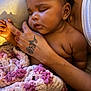 Niari is registered to the contest to win money with this photo: baby, sleeping, tattoo, hand, blanket, cozy, curly_hair, earring, skin, person, adult, holding, comfort, cuddle, indoor, closeup, tender, affection, relaxation, warmth