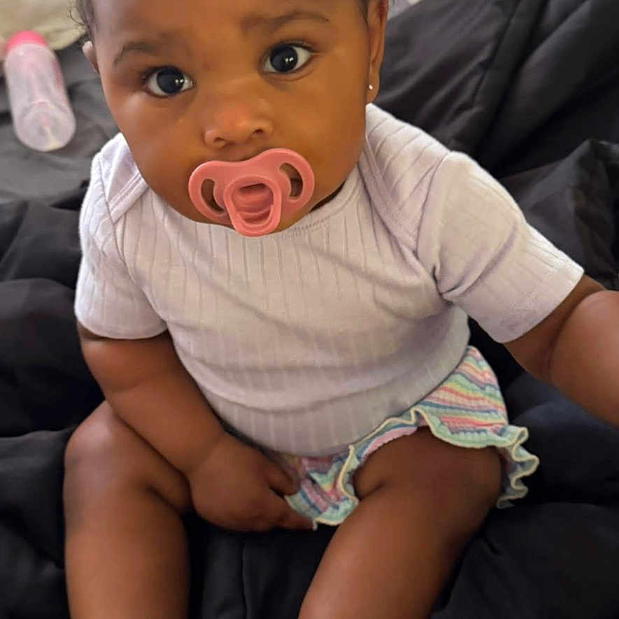 Niari joined the competition — help win amazing prizes! baby, blanket, bottle, child, clothing, curly_hair, cute, expression, face, foot, hand, indoors, infant, pacifier, person, pigtails, portrait, sitting, skin, young