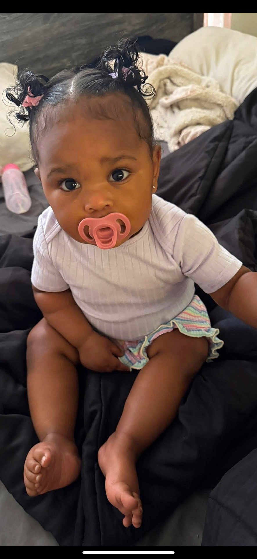 Niari joined the competition — help win amazing prizes! baby, child, pacifier, pigtails, curly_hair, sitting, blanket, indoors, clothing, cute, infant, bottle, person, skin, foot, hand, face, expression, portrait, young