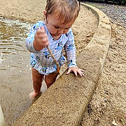 Lilia is registered to the contest to win money with this photo: toddler, child, water, sand, stick, swimsuit, outdoor, park, trees, concrete, curved_edge, playing, nature, daylight, young_child, barefoot, muddy, puddle, fence, grass