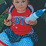 toddler, child, bottle, snack, chair, red_clothing, blue_clothing, white_clothing, stars_pattern, smile, hair_tie, outdoor, grass, baby_shoes, person, cute, portrait, sitting, fun, casual