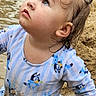 toddler, child, beach, sand, water, blue_outfit, long_sleeves, cartoon_pattern, wet_hair, curious_expression, looking_up, playful, summer, outdoor, young_child, portrait, muddy, hand_on_sand, cute, daylight