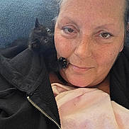 Loki is registered to the contest to win money with this photo: woman, kitten, black_cat, face, paw, close_up, snuggling, blanket, jacket, brown_eyes, freckles, indoor, pet, cute, affection, cozy, resting, feline, human, companion