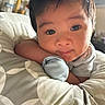 baby, infant, face, close_up, cushion, pattern, hand, mitten, soft_lighting, indoor, portrait, curious_eyes, resting, cute, child, young, cozy, warm_tones, person, skin
