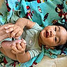 baby, child, infant, blanket, penguin_pattern, feet, hands, onesie, dinosaur, smiling, happy, lying_down, cute, soft_texture, indoors, portrait, toddler, playful, colorful, expression