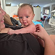 Rian is registered to the contest to win money with this photo: adult, baby, background, black_clothing, child, curious, expression, face, floor, furniture, hand, holding, home, human, indoor, living_room, person, shirt, skin, wide_eyes