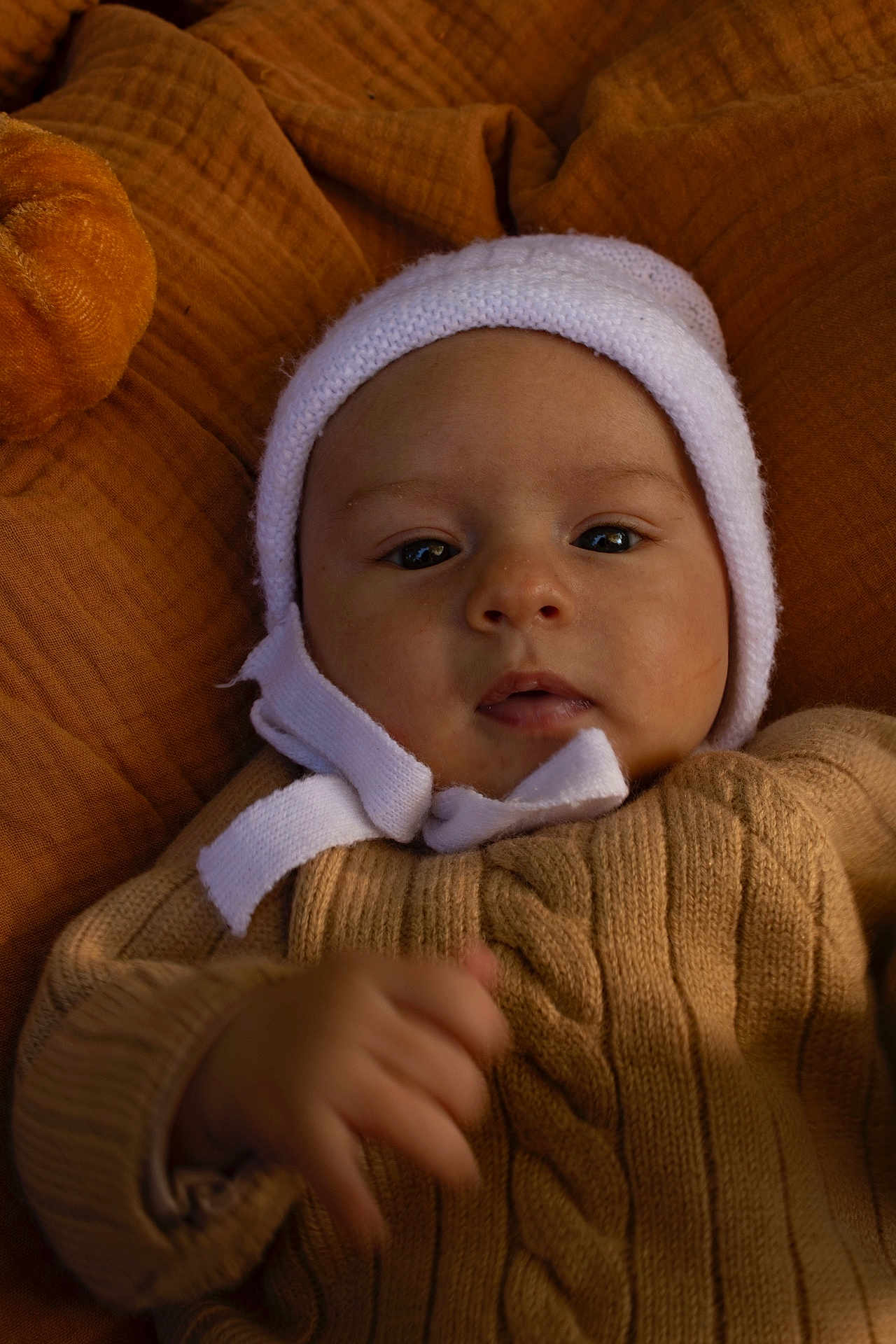 Charles a rejoint le concours — aidez-le/la à gagner de superbes lots ! baby, infant, knitted_sweater, white_bonnet, blanket, soft_texture, closeup, portrait, warm_colors, cute, child, young, face, hand, cozy, indoors, expression, resting, skin, headwear