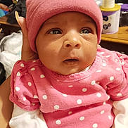 Ra'Taejah is registered to the contest to win money with this photo: baby, infant, pink_hat, pink_clothing, polka_dot, white_sleeves, hand, face, eyes, indoor, person, newborn, portrait, clothing, headwear, expression, supporting_hand, cozy, warm, closeup