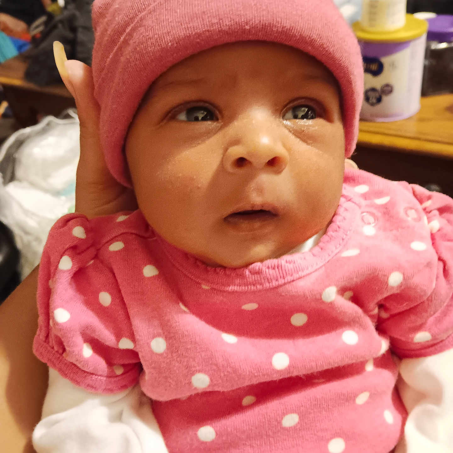 Ra'Taejah is registered to the contest to win money with this photo: baby, closeup, clothing, cozy, expression, eyes, face, hand, headwear, indoor, infant, newborn, person, pink_clothing, pink_hat, polka_dot, portrait, supporting_hand, warm, white_sleeves