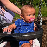 Amalia-Estelle joined the competition — help win amazing prizes! baby, pacifier, swing, blue_outfit, tattoo, arm, park, playground, grass, sunlight, child, outdoor, person, holding, chain, summer, cute, infant, seat, blanket