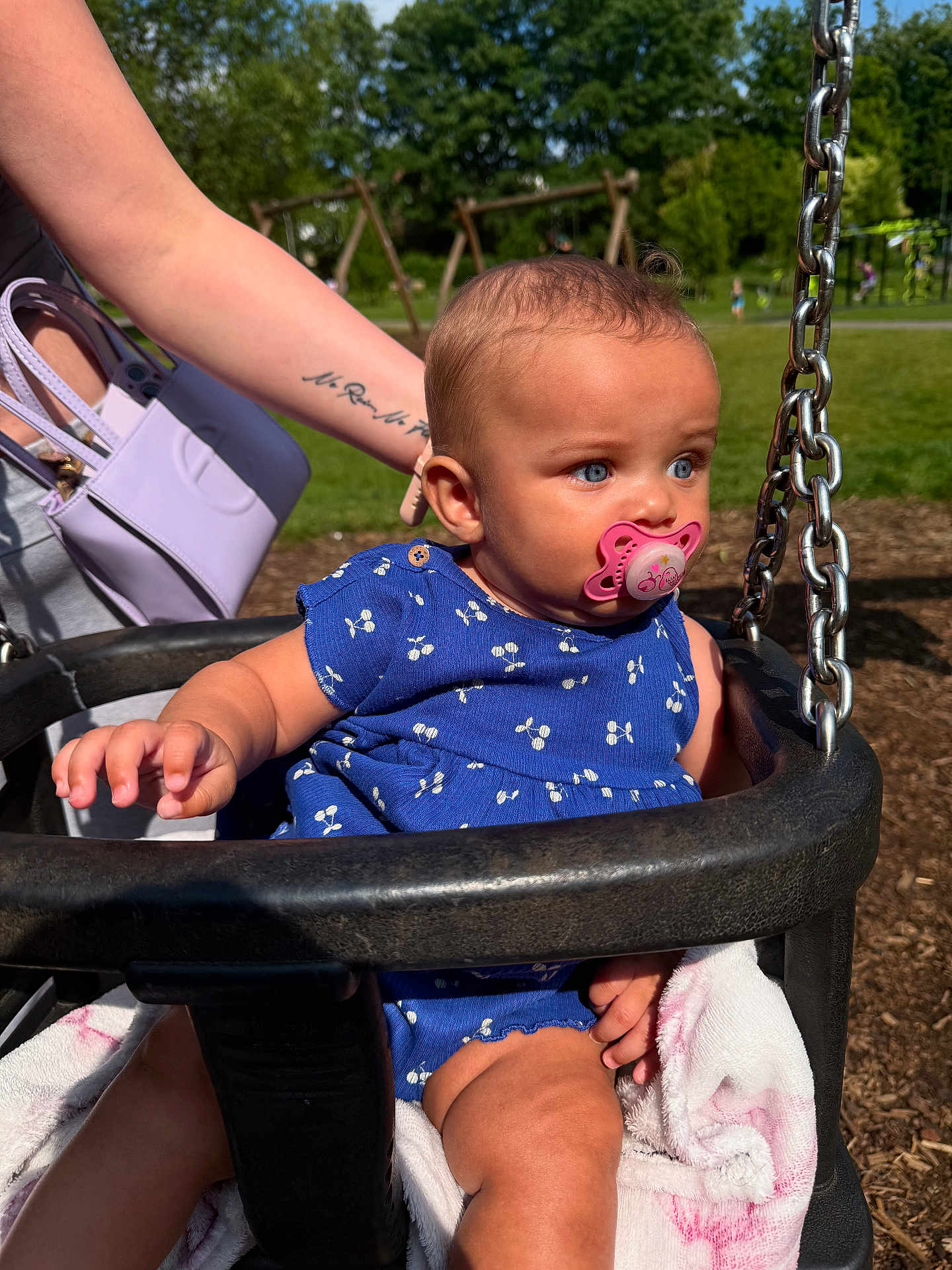Amalia-Estelle joined the competition — help win amazing prizes! baby, pacifier, swing, blue_outfit, tattoo, arm, park, playground, grass, sunlight, child, outdoor, person, holding, chain, summer, cute, infant, seat, blanket