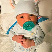 Matthias joined the competition — help win amazing prizes! baby, bed, blanket, child, cozy, cute, expression, face, hands, hat, indoors, infant, lying_down, newborn, pacifier, pajamas, person, sleepwear, soft, wearing