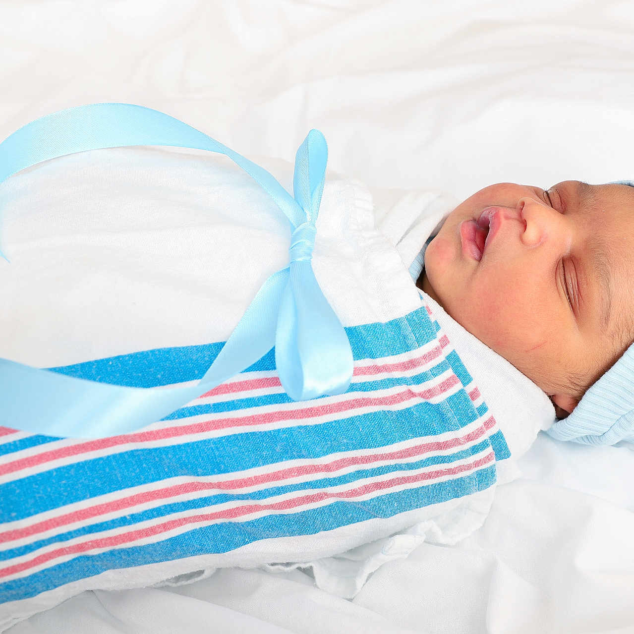 Kaiyzer is registered to the contest to win money with this photo: newborn, baby, sleeping, wrapped, blanket, blue_ribbon, hat, infant, peaceful, soft, white_background, portrait, cute, child, resting, closeup, swaddled, newborn_clothing, baby_boy, indoors
