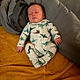 baby, newborn, sleeping, footed_pajamas, dinosaur_print, blanket, gray_bedding, mustard_blanket, cozy, lying_down, peaceful, face, closed_eyes, hands, feet, soft_texture, hair, indoor, portrait, sleepwear