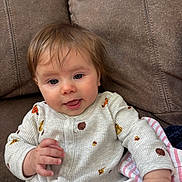 Catherine joined the competition — help win amazing prizes! baby, child, infant, couch, onesie, white_clothing, brown_hair, smiling, indoor, cozy, soft_fabric, blanket, striped_blanket, cute, portrait, seated, hand, face, curious, happy