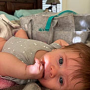 Catherine is registered to the contest to win money with this photo: baby, infant, child, bed, hand, face, eyes, fingers, sucking, lying_down, blanket, clothing, hair, indoor, soft_light, wooden_headboard, fabric_bag, cozy, curious, portrait