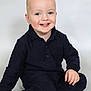 toddler, child, smiling, blue_eyes, blonde_hair, sitting, navy_clothing, long_sleeves, pants, black_socks, studio_photo, portrait, happy, cute, indoor, isolated_background, young_child, casual_wear, face, person