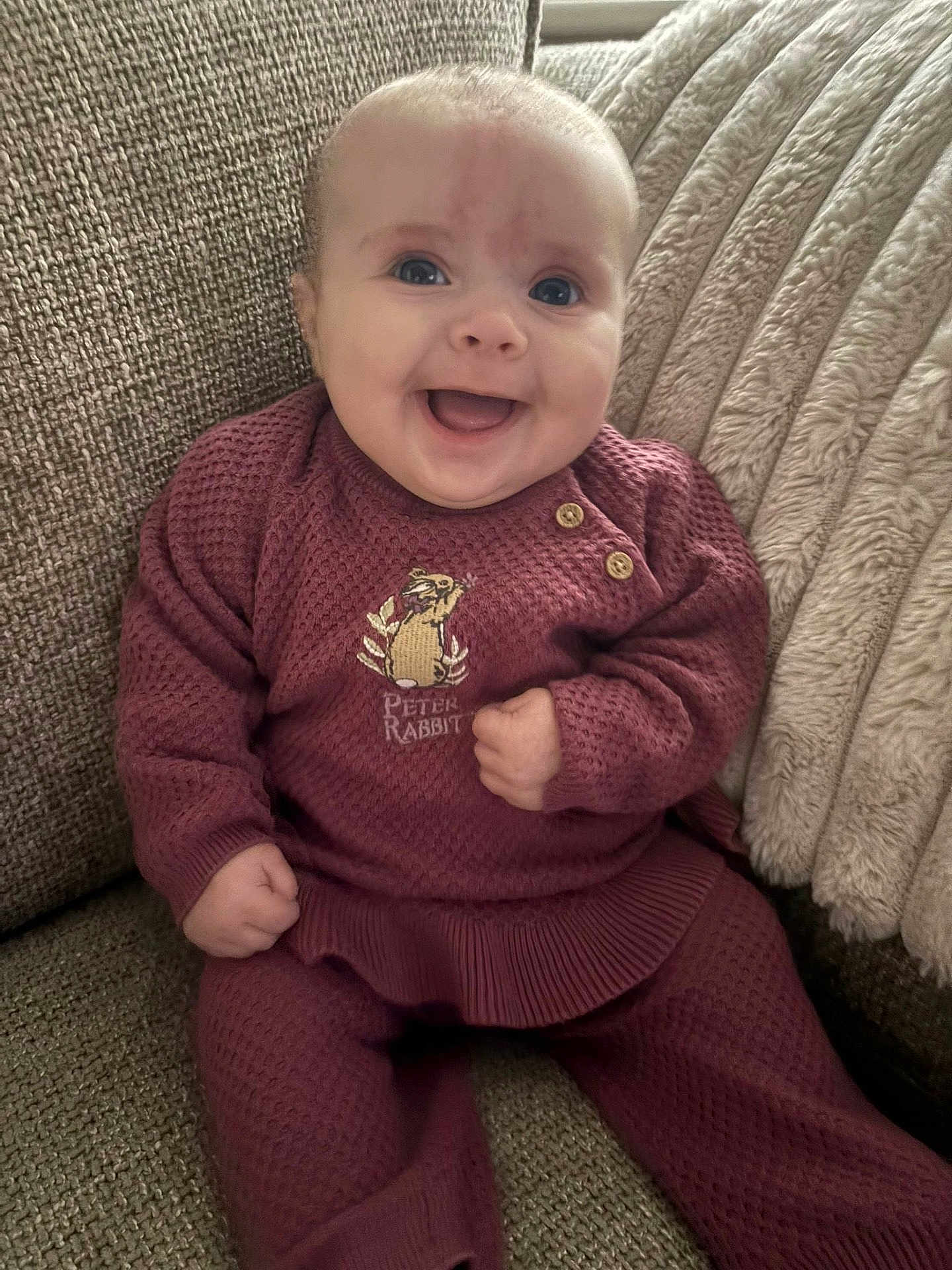 Lenie joined the competition — help win amazing prizes! baby, infant, smiling, knitted_clothing, maroon_outfit, peter_rabbit, couch, blanket, happy, sitting, portrait, face, child, home_interior, cozy, cute, furniture, person, comfortable, young_child