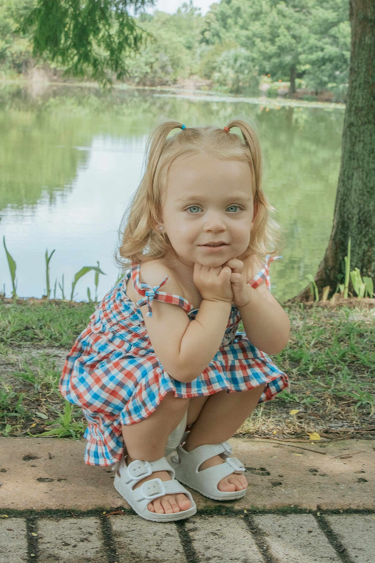 Lennon joined the competition — help win amazing prizes! child, toddler, blonde_hair, pigtails, dress, checkered_pattern, white_sandals, outdoor, pond, greenery, grass, tree, path, summer, nature, cute, portrait, squatting, young_child, daylight