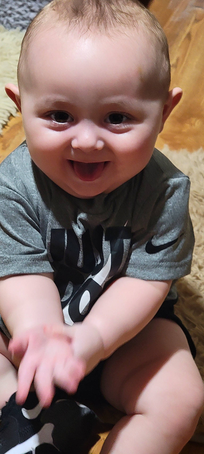 Damon is registered to the contest to win money with this photo: baby, babylaughing, bodypart, clothing, face, finger, footwear, hand, happy, hardwood, head, laughing, person, photography, portrait, shoe, sitting, smile, t_shirt, wood