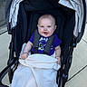 Berkley is registered to the contest to win money with this photo: baby, child, infant, stroller, smiling, portrait, outdoor, blanket, purple_shirt, harness, seated, blue_eyes, face, head, happy, pavement, walkway, carriage, sunlight, photography