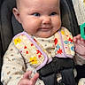 baby, infant, child, smiling, portrait, car_seat, safety_harness, buckle, floral_clothing, bib, outdoor, vehicle, seated, face, blue_eyes, fair_skin, hand, reaching, close_up, happy