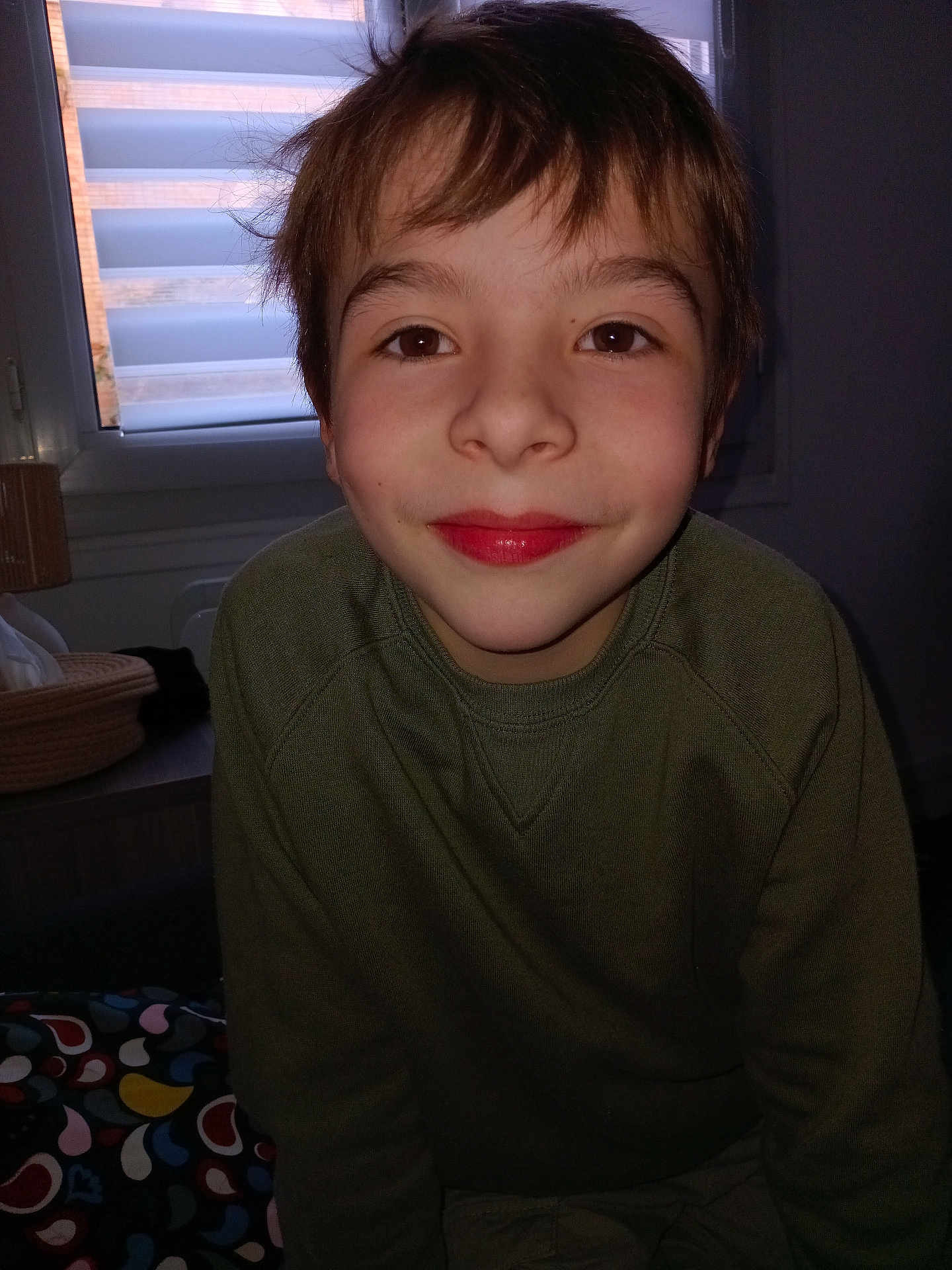 Matheo a rejoint le concours — aidez-le/la à gagner de superbes lots ! child, boy, smile, face, indoors, window, green_sweater, hair, young, portrait, person, casual_clothing, home, background, expression, sitting, happy, childhood, light, cozy