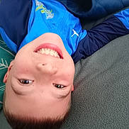 Matheo a rejoint le concours — aidez-le/la à gagner de superbes lots ! child, smiling, upside_down, blue_jacket, puma_logo, face, couch, blanket, indoor, happy, casual_clothing, head, person, relaxed, young, playful, portrait, cozy, home, resting