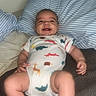 baby, infant, smiling, onesie, animal_print, pillow, striped_pillow, blanket, lying_down, happy, child, cute, indoors, soft_fabric, skin, foot, hand, face, cheerful, room