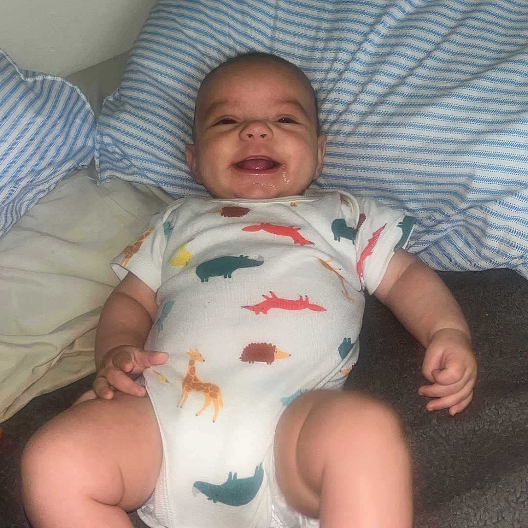 Adrean joined the competition — help win amazing prizes! baby, infant, smiling, onesie, animal_print, pillow, striped_pillow, blanket, lying_down, happy, child, cute, indoors, soft_fabric, skin, foot, hand, face, cheerful, room