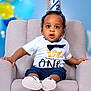 baby, child, crown, half_birthday, chair, white_shirt, navy_shorts, baby_shoes, surprised_expression, indoor, portrait, celebration, balloons, soft_lighting, cute, sitting, face, headband, infant, studio_photo