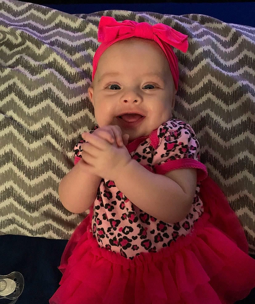 Clementine is registered to the contest to win money with this photo: baby, baby_toddler_clothing, facial_expression, finger, fun, hairstyle, happy, headwear, iris, lip, organ, outerwear, person, photograph, pink, purple, skin, sleeve, smile, textile