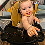 baby, high_chair, food, spaghetti, messy, indoor, playpen, child, smiling, face, hand, diaper, floor, wooden_floor, background, toy, seat, person, happy, reaching