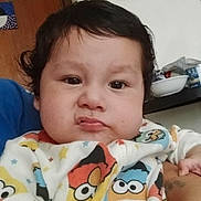 Tobias is registered to the contest to win money with this photo: baby, child, face, expression, indoor, clothing, onesie, colorful, curly_hair, pout, kitchen, counter, bowl, container, person, portrait, young_child, cute, skin, hand