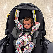 Mckinleigh joined the competition — help win amazing prizes! baby, infant, child, car_seat, floral_outfit, onesie, sitting, lying_down, arms_raised, blue_eyes, brown_hair, face, portrait, indoor, floor, safety_harness, travel, vehicle, parent_hand, colorful_clothing