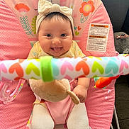 Mia is registered to the contest to win money with this photo: baby, infant, child, smiling, tongue_out, headband, bow, pink, baby_bouncer, toy_bar, colorful, hearts, flowers, plush_toy, cute, happy, sitting, indoors, closeup, playful
